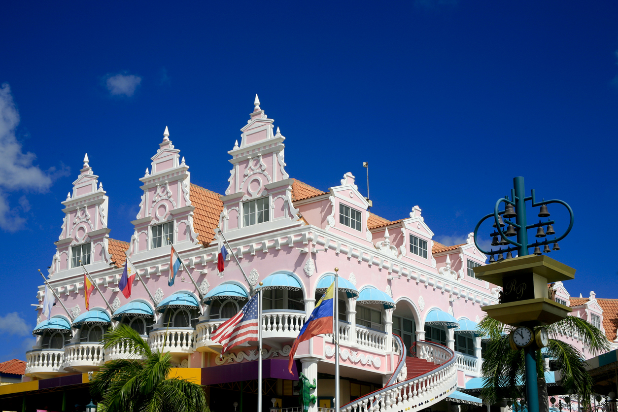 The pink iconic Royal Plaza, Oranjestad, Aruba with the bell tower on the right. An outdoor staircase leads onto the second floor. Deep blue sky.