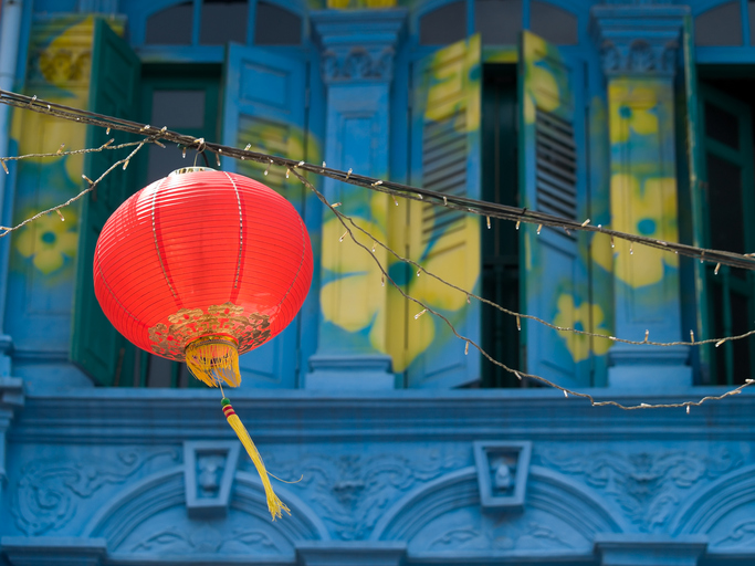 Hanging Red Lantern over Street in Chinatown against a blue facade painted with yellow flowers