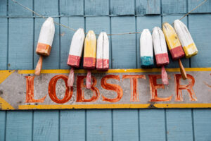 Buoys hang above a faded sign promoting losters